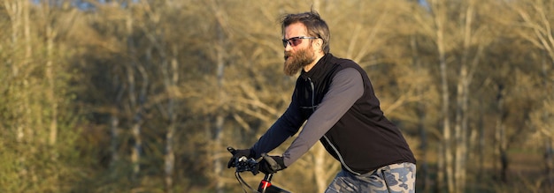 Sport brute bebaarde man op een moderne mountainbike fietser op de groene heuvels in de lente