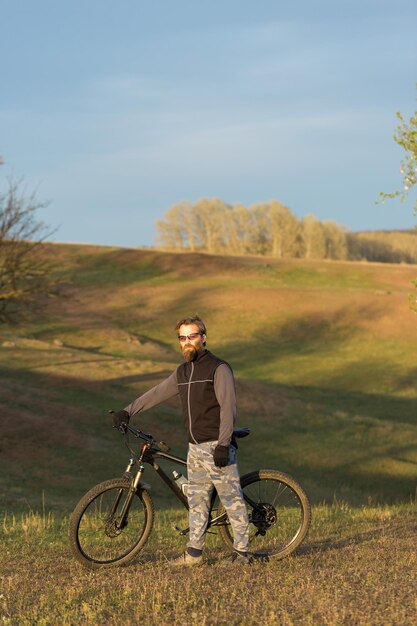 Sport brute bebaarde man op een moderne mountainbike Fietser op de groene heuvels in de lente