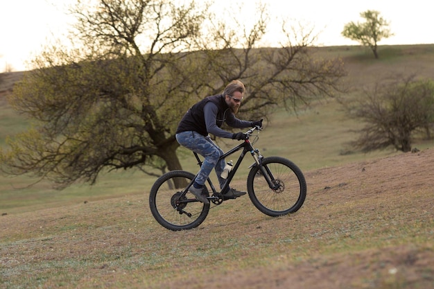 Sport brute bebaarde man op een moderne mountainbike Fietser op de groene heuvels in de lente