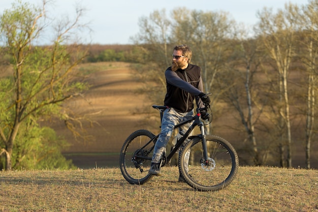 Sport brute bebaarde man op een moderne mountainbike. Fietser op de groene heuvels in het voorjaar.