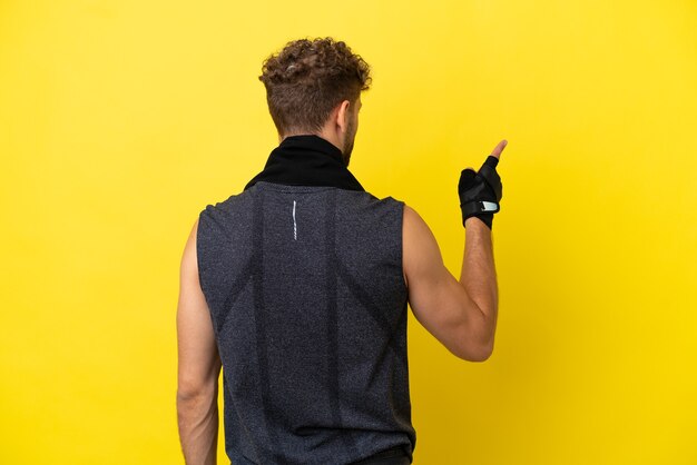 Sport caucasian man isolated on yellow background pointing back with the index finger