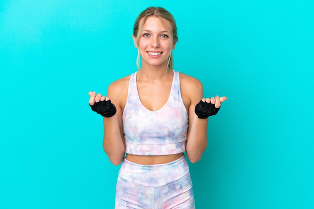 Sport caucasian woman isolated on blue background making money gesture