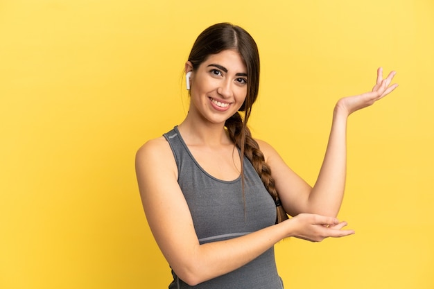 Sport caucasian woman isolated on yellow background extending hands to the side for inviting to come
