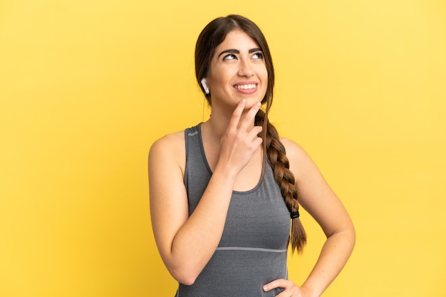 Sport caucasian woman isolated on yellow background looking up while smiling