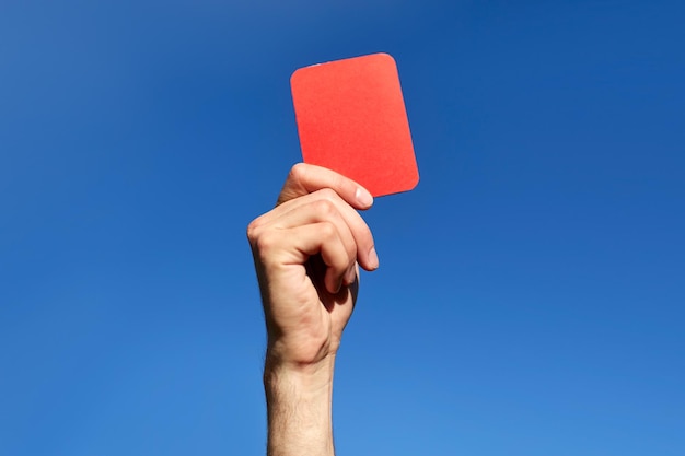 Sport, caution, game and people - close up of referee hands with whistle showing red card on football field