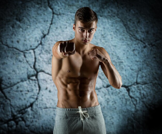 sport, competition, strength and people concept - young man in fighting or boxing position over concrete wall background