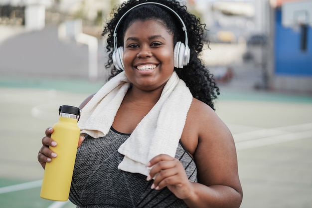 Sport curvy black woman listening music with headphones - Focus on face