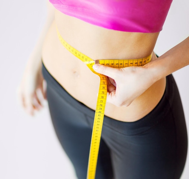 sport and diet concept - trained belly with measuring tape