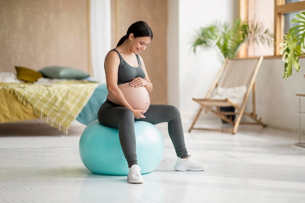 Photo sport during pregnancy beautiful pregnant female sitting on fitball and embracing belly