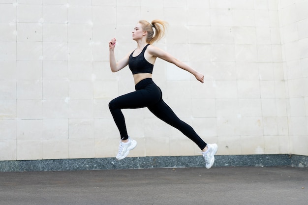 Sport en fitness concept jonge volwassen blanke vrouwelijke atleet springen hoog buiten grijze staart muur achtergrond sportieve vrouw springen oefeningen buiten gezonde levensstijl motivatie