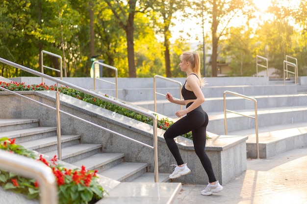 Sport en fitness fitte vrouw traplopen zomer zonnige ochtend Kaukasische atletische vrouw joggen buiten cardiotraining actieve gezonde levensstijl gekleed zwart sportkleding motivatie concept