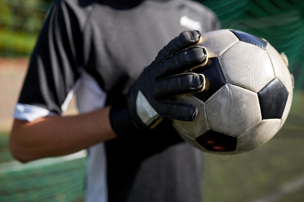 sport en mensen - close-up van voetballer of keeper die bal vasthoudt bij voetbaldoel op het veld