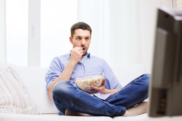 Sport, eten, geluk en mensenconcept - man die tv kijkt en thuis popcorn eet