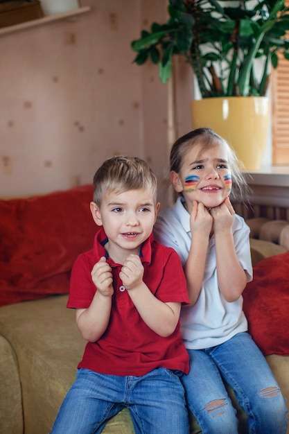 Sport fan with colored cheeks sitting on sofa, watching sport games and cheering for team online at home, real emotions, sports event and safe fun supporting, social distant cheering during lockdown