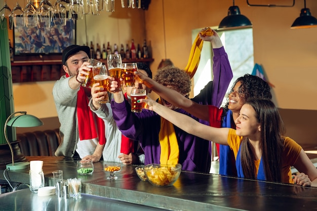 Поклонники спорта аплодируют в баре, пабе и пьют пиво, пока идет чемпионат, соревнования. Многонациональная группа друзей.