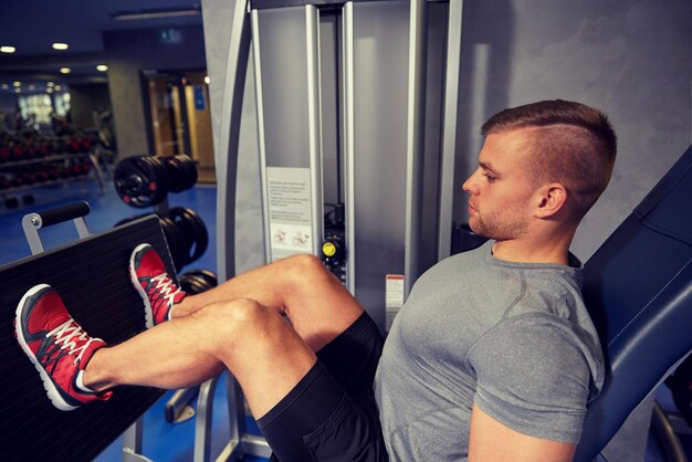 sport, fitness, bodybuilding, lifestyle and people concept - man exercising and flexing leg muscles on gym machine