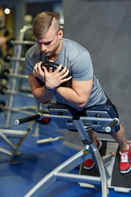 Foto concetto di sport, fitness, bodybuilding, stile di vita e persone - giovane che flette i muscoli della schiena e addominali sulla panca in palestra