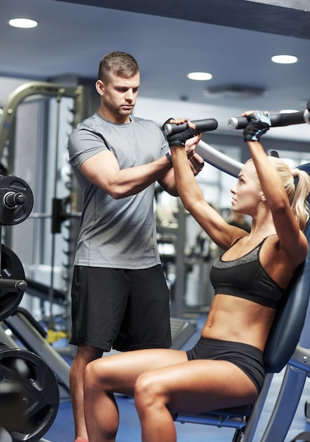 sport, fitness, bodybuilding, teamwork en mensen concept - jonge vrouw en personal trainer buigen spieren op gym machine