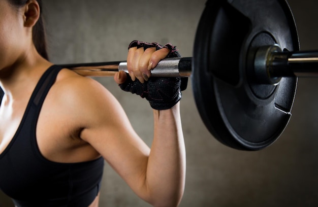 Foto concetto di sport, fitness, bodybuilding, sollevamento pesi e persone - primo piano di una giovane donna con i muscoli che flettono il bilanciere in palestra