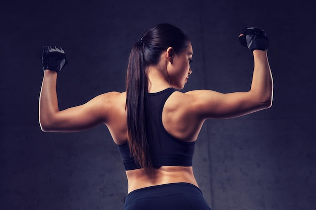 스포츠, 피트니스, 보디 빌딩, 역도 및 사람들의 개념 - 체육관에서 근육을 구부리는 젊은 여성