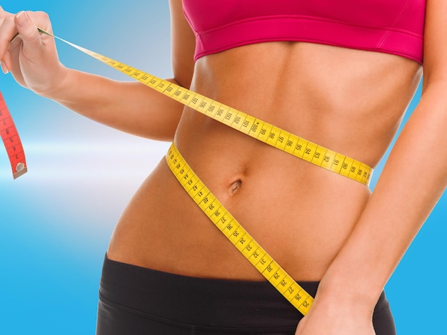 sport, fitness and diet concept - close up of trained belly with measuring tape