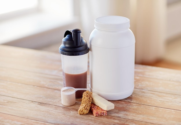 Photo sport, fitness, diet and food concept - close up of jar, protein shake bottle and muesli bars on wooden table