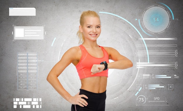 Foto sport-, fitness- en technologieconcept - gelukkige lachende jonge vrouw met hartslagmeter of smartwatch over grijze betonnen achtergrond