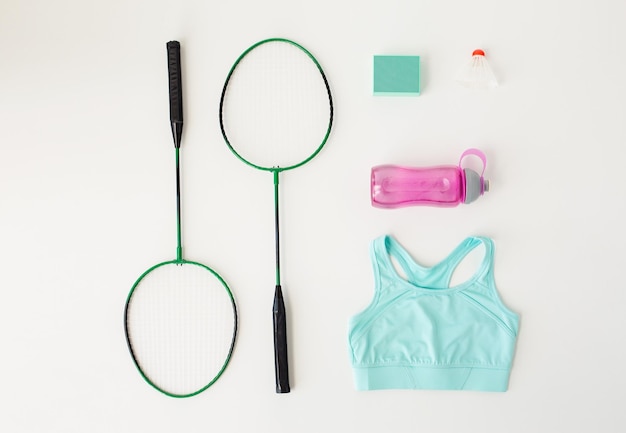 sport, fitness, healthy lifestyle and objects concept - close up of badminton rackets with speaker and sports stuff over white background