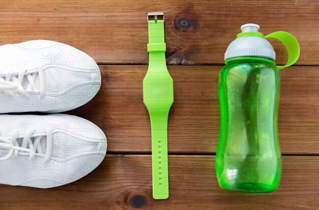 sport, fitness, healthy lifestyle and objects concept - close up of sneakers, bracelet and water bottle on wooden floor