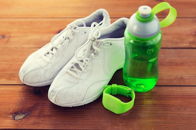 Sport, fitness, healthy lifestyle and objects concept - close up of sneakers, bracelet and water bottle on wooden floor