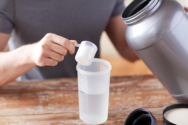 sport, fitness, healthy lifestyle and people concept - close up of man with jar and bottle preparing protein shake