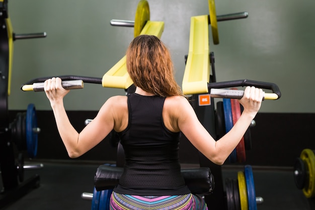 Sport, fitness, levensstijl en mensenconcept - sluit omhoog van jonge vrouwen buigende spieren op de machine van de kabelgymnastiek