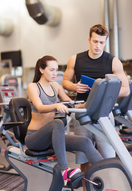 sport, fitness, levensstijl, technologie en mensenconcept - vrouw met trainer die op hometrainer in gymnastiek uitwerkt