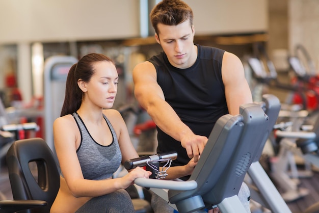 Sport, fitness, levensstijl, technologie en mensenconcept - vrouw met trainer die op hometrainer in gymnastiek uitwerkt