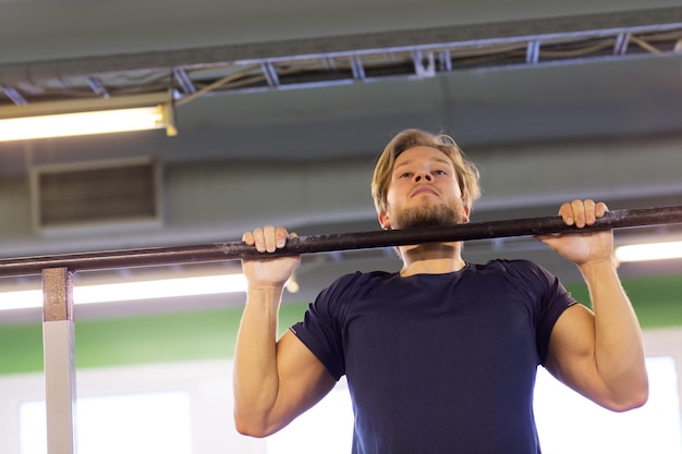 Foto sport, fitness, lichaamsbeweging en mensenconcept - man die pull-ups doet op een horizontale balk in de sportschool