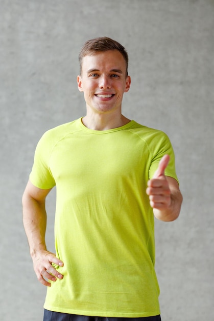 Concetto di sport, fitness, stile di vita e persone - uomo sorridente che mostra i pollici in su in palestra