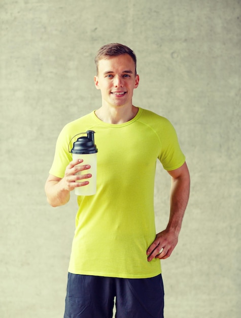 sport, fitness, lifestyle and people concept - smiling man with protein shake bottle in gym