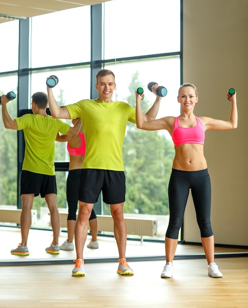 Photo sport, fitness, lifestyle and people concept - smiling man and woman with dumbbells exercising in gym