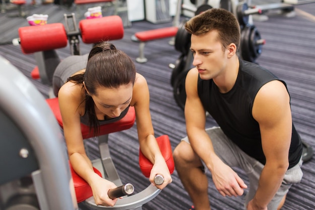 sport, fitness, lifestyle and people concept - young woman and personal trainer flexing leg muscles on gym machine