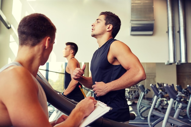 Foto sport, fitness, lifestyle, technologie en mensen concept - mannen met personal trainer trainen op de loopband in de sportschool