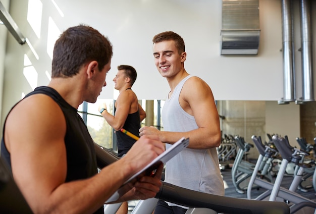 sport, fitness, lifestyle, technologie en mensen concept - mannen met personal trainer trainen op de loopband in de sportschool