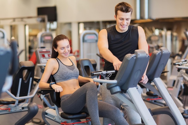 Sport, fitness, stile di vita, tecnologia e concetto di persone - donna felice con trainer che si allena sulla cyclette in palestra