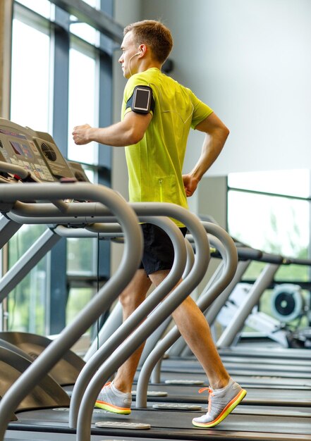 sport, fitness, lifestyle, technology and people concept - man with smartphone and earphones exercising on treadmill in gym