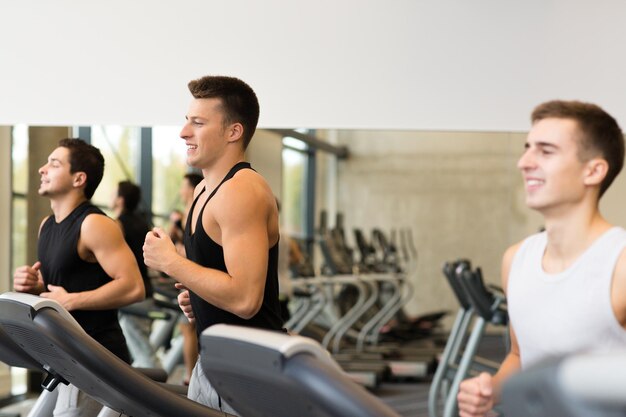 sport, fitness, lifestyle, technology and people concept - smiling men exercising on treadmill in gym