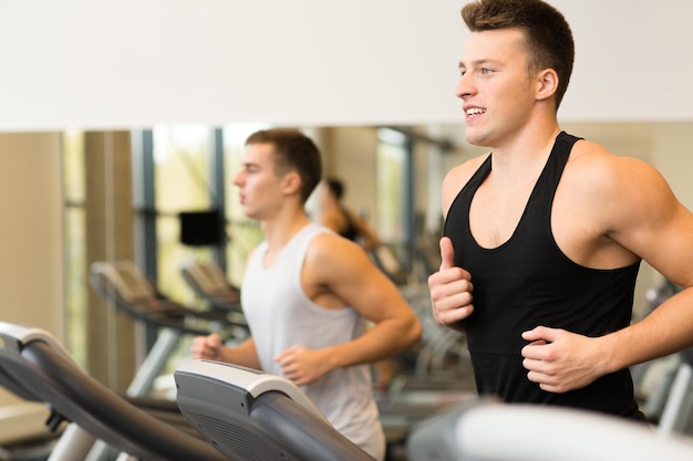 Concetto di sport, fitness, stile di vita, tecnologia e persone - uomini sorridenti che si esercitano sul tapis roulant in palestra