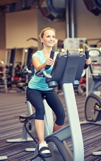 sport, fitness, lifestyle, technology and people concept - smiling woman exercising on exercise bike in gym