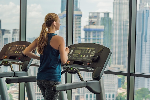 Sport, fitness, lifestyle, technology and people concept - woman exercising on treadmill in gym against the background of a big city