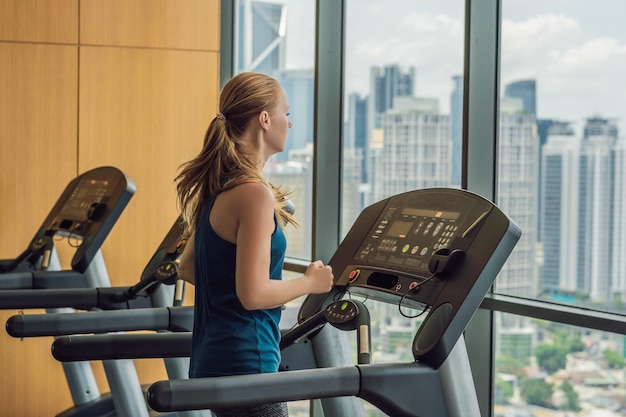 Sport, fitness, lifestyle, technology and people concept - woman exercising on treadmill in gym against the background of a big city