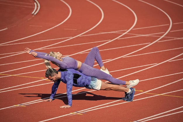 写真 一緒にトレーニングするスポーツフィットネスの男性と女性は板に立って、スポーツウェアのスポーツトレーニングを身に着けている屋外スタジアムの競馬場で腕立て伏せをします