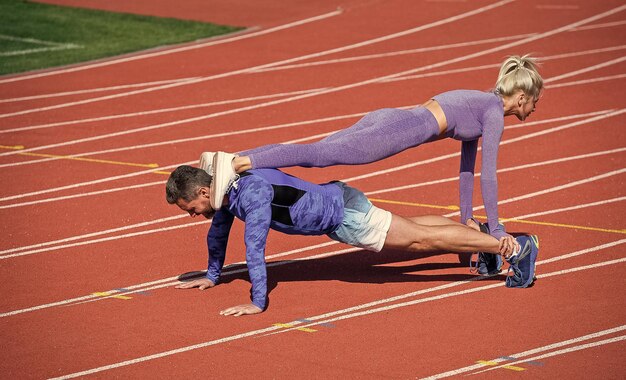 スポーツフィットネスの男女が一緒にトレーニングをし、板に立ち、スポーツウェアの健康的なライフスタイルを身に着けた屋外スタジアムの競馬場で腕立て伏せをする